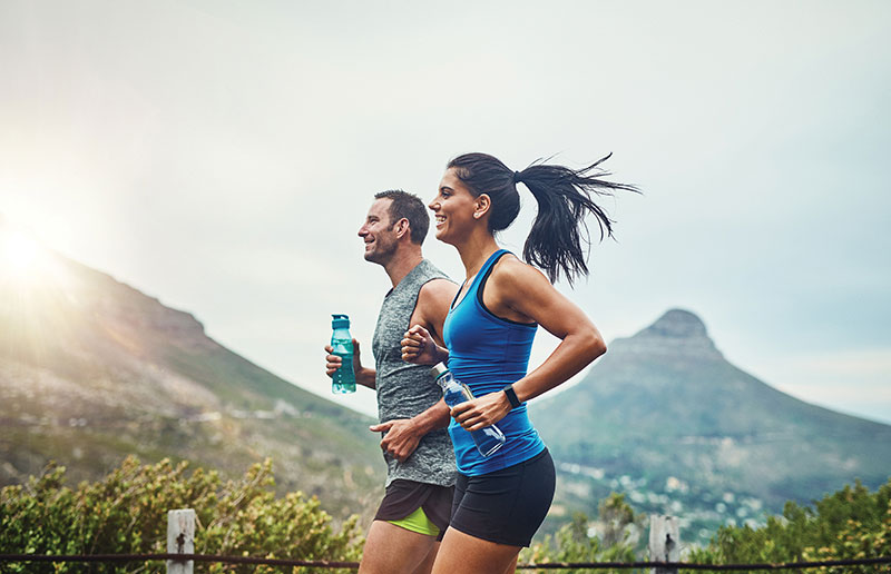 Athletic man and woman jogging across mountain landscape, holding water bottles