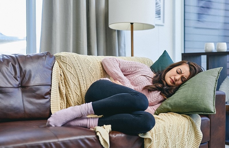 Woman lying on the couch, clutching her stomach